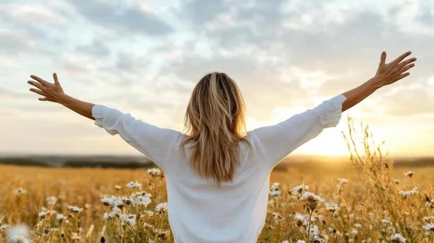 Vrouw met open armen in een zonnig veld